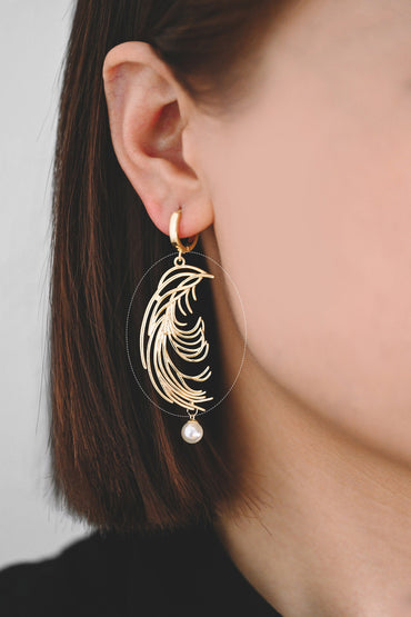 May include: Gold hoop earrings with a dangling pearl and a feather-shaped design.