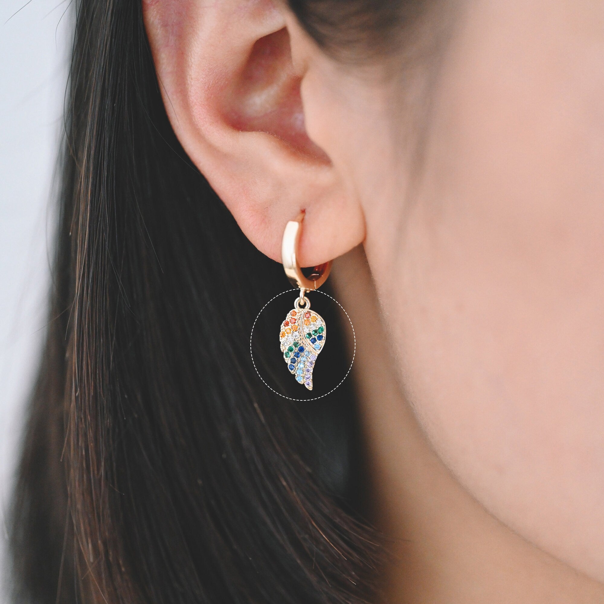 May include: A gold hoop earring with a dangling charm in the shape of a leaf. The leaf is covered in colorful rhinestones.