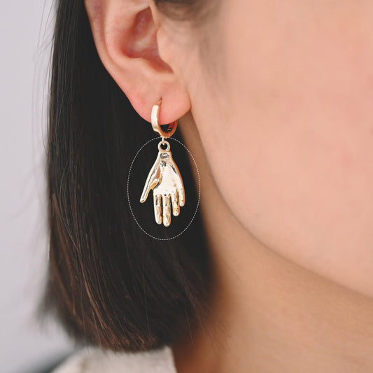 May include: Gold hoop earrings with a dangling hand charm.
