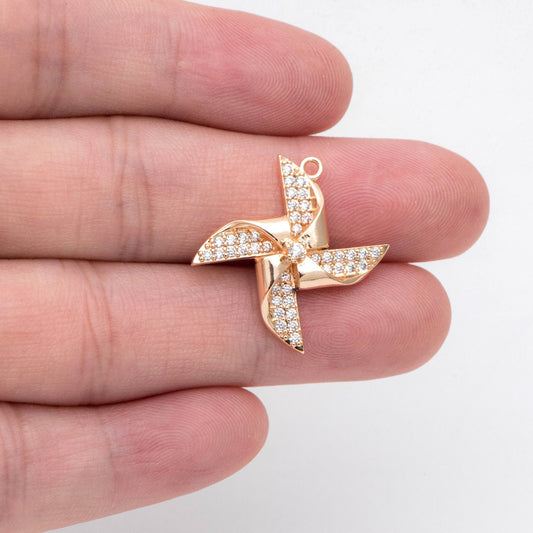 May include: A gold-toned pinwheel charm with clear rhinestones. The pinwheel has four blades and a center stone.