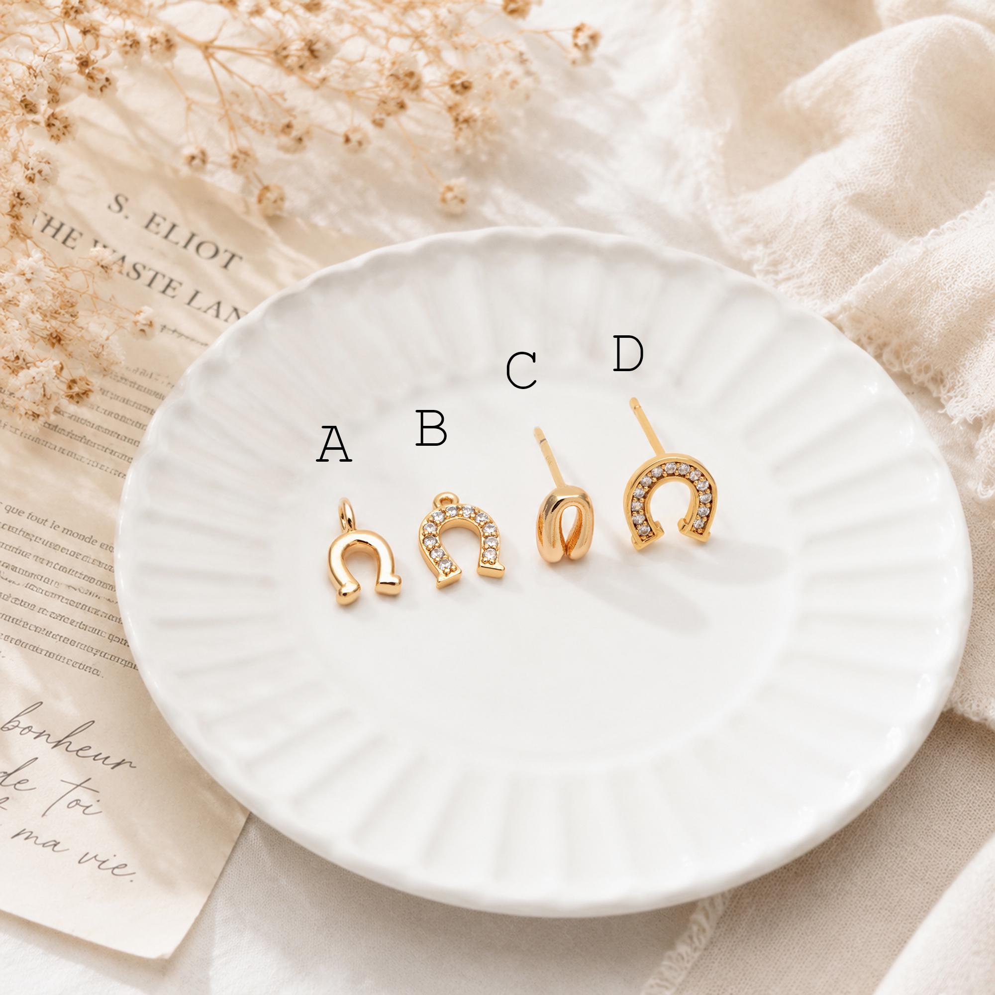 May include: Four gold-colored horseshoe-shaped jewelry pieces on a white plate. Item A is a pendant, B is a charm with small clear stones, C is a stud earring, and D is a stud earring with clear stones.