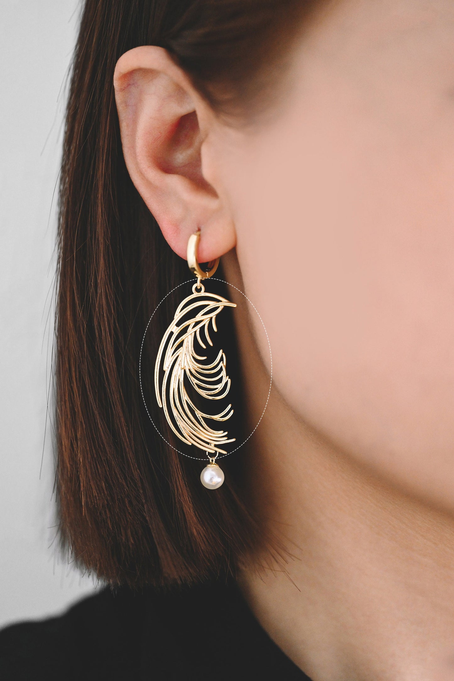May include: Gold hoop earrings with a dangling pearl and a feather-shaped design.
