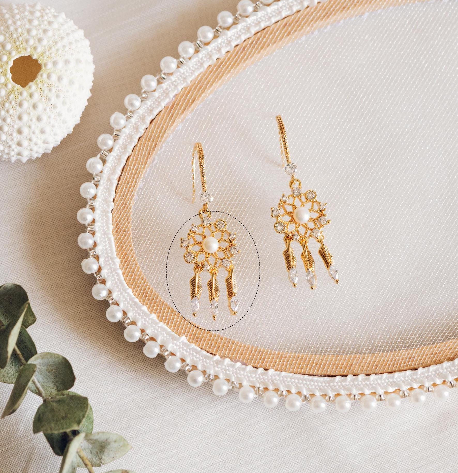 May include: Two gold dangle earrings with a pearl center and clear crystal accents. The earrings are displayed on a white pearl trim oval frame.