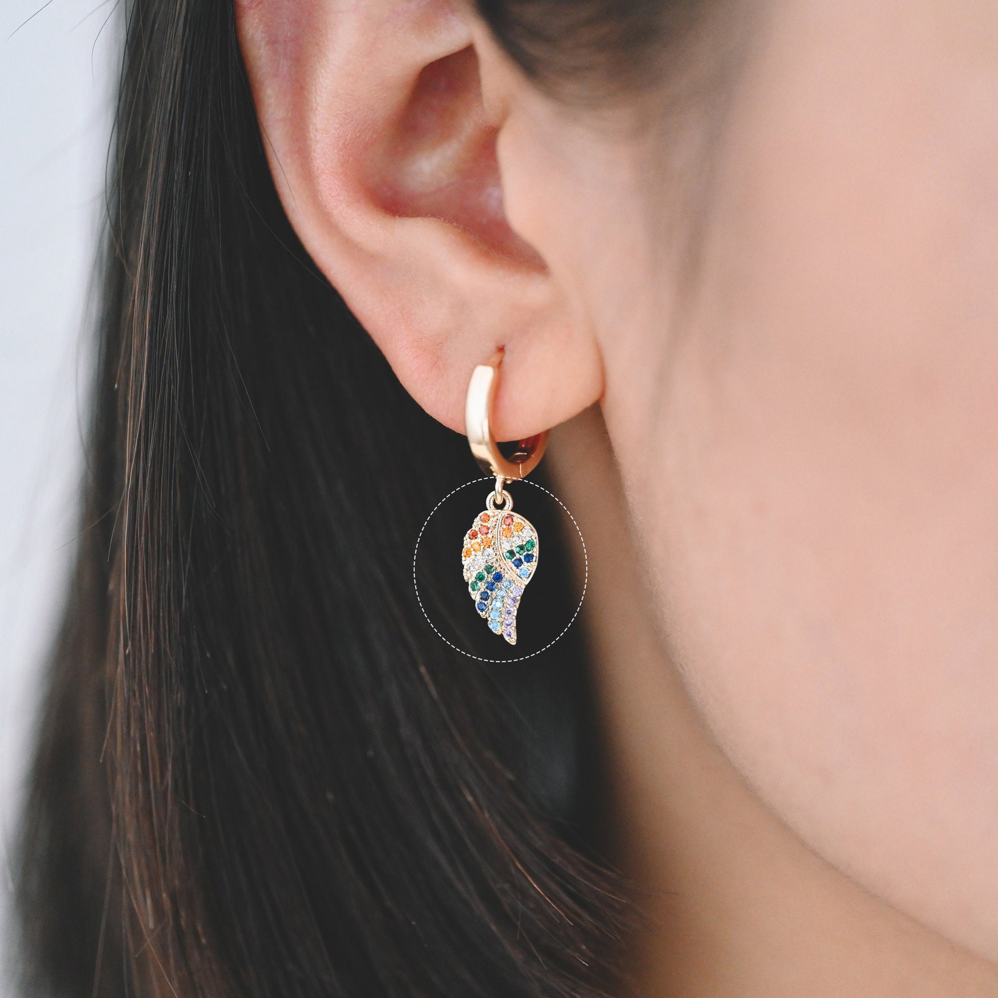 May include: A gold hoop earring with a dangling charm in the shape of a leaf. The leaf is covered in colorful rhinestones.