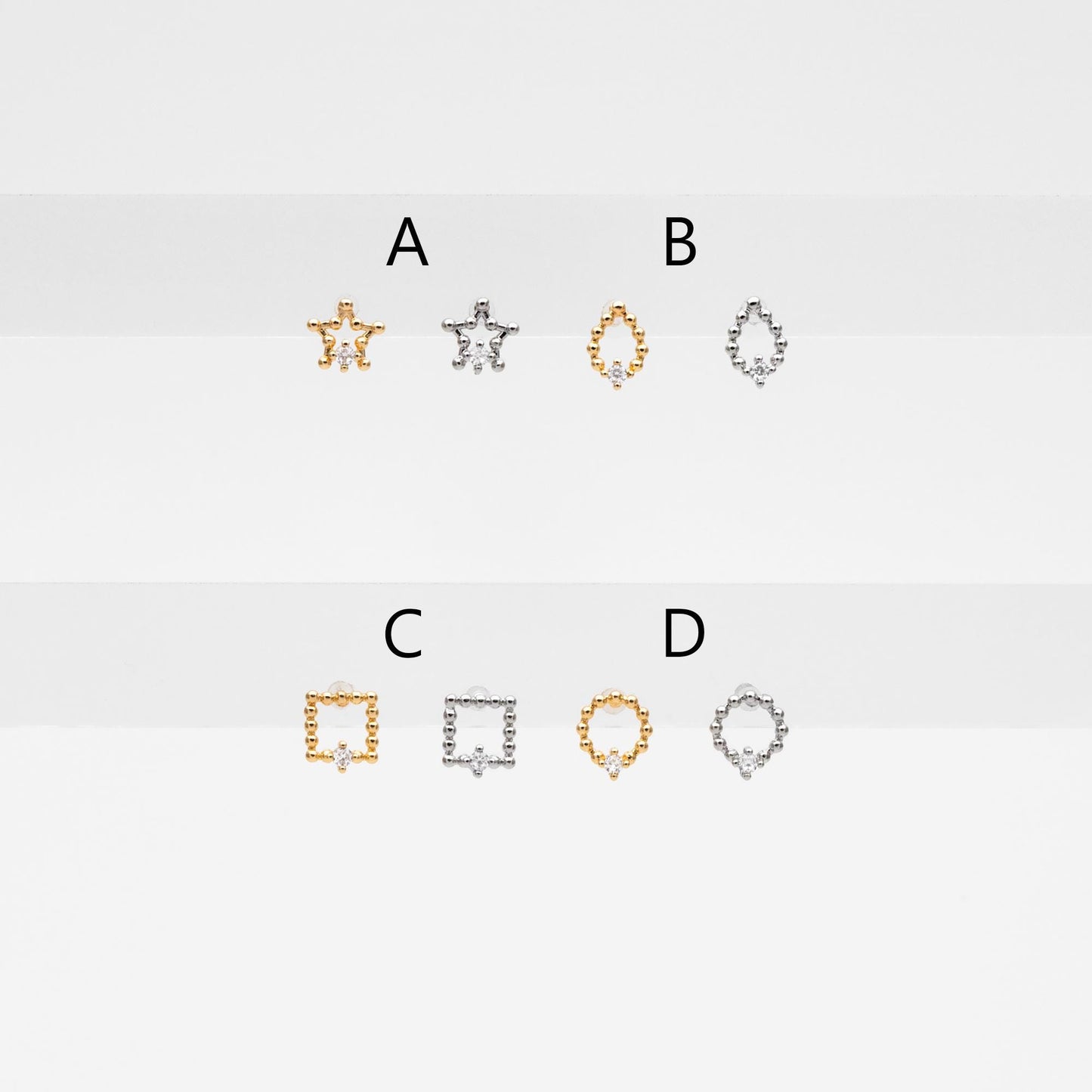 May include: Six small gold and silver jewelry pieces with a single diamond in the center of each piece. The pieces are shaped like a star, a teardrop, a square, and a circle. The pieces are labeled with the letters A, B, C, and D.