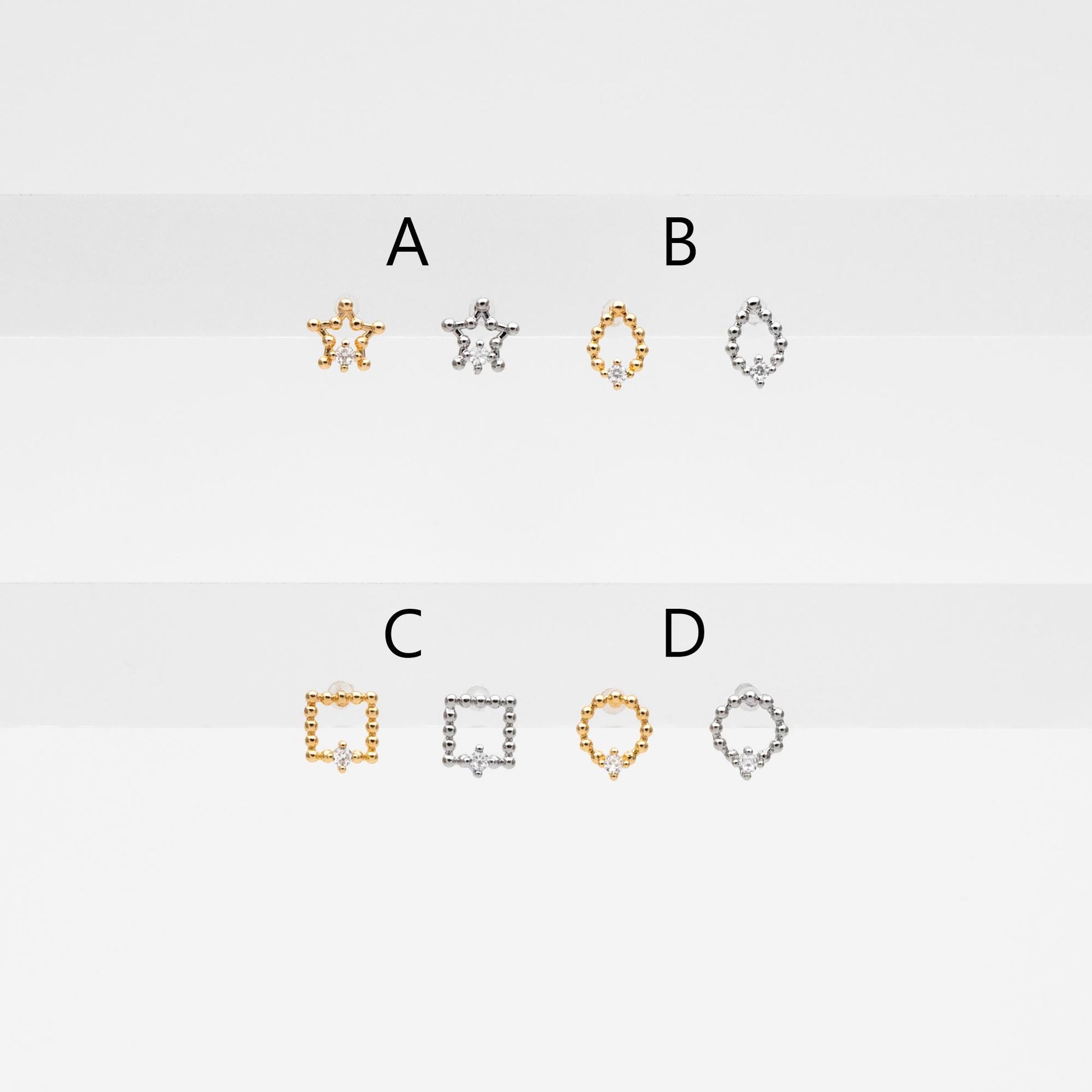 May include: Six small gold and silver jewelry pieces with a single diamond in the center of each piece. The pieces are shaped like a star, a teardrop, a square, and a circle. The pieces are labeled with the letters A, B, C, and D.