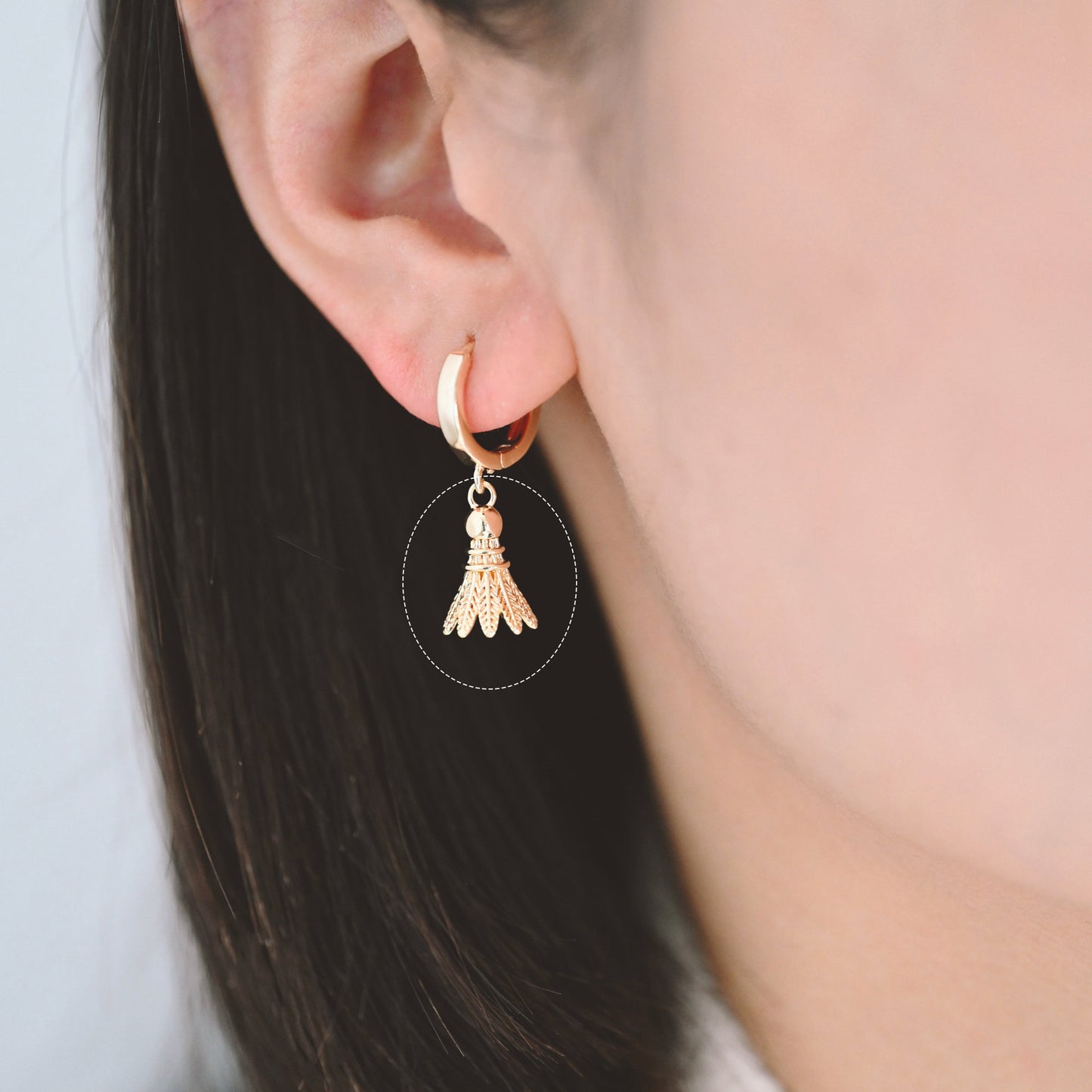 May include: Gold hoop earrings with a badminton shuttlecock charm hanging from each hoop.