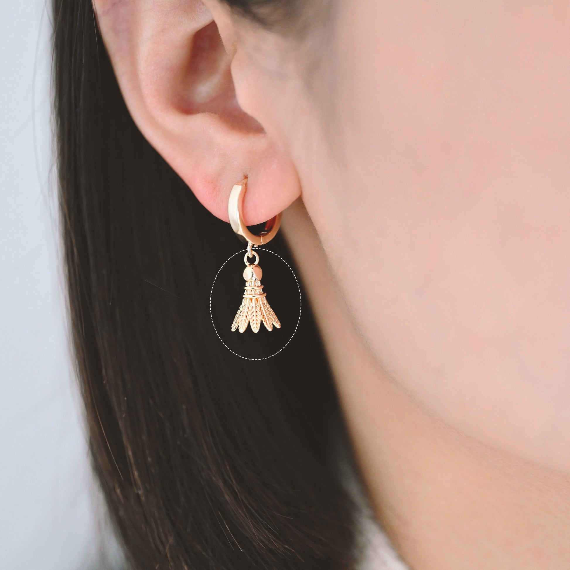 May include: Gold hoop earrings with a badminton shuttlecock charm hanging from each hoop.
