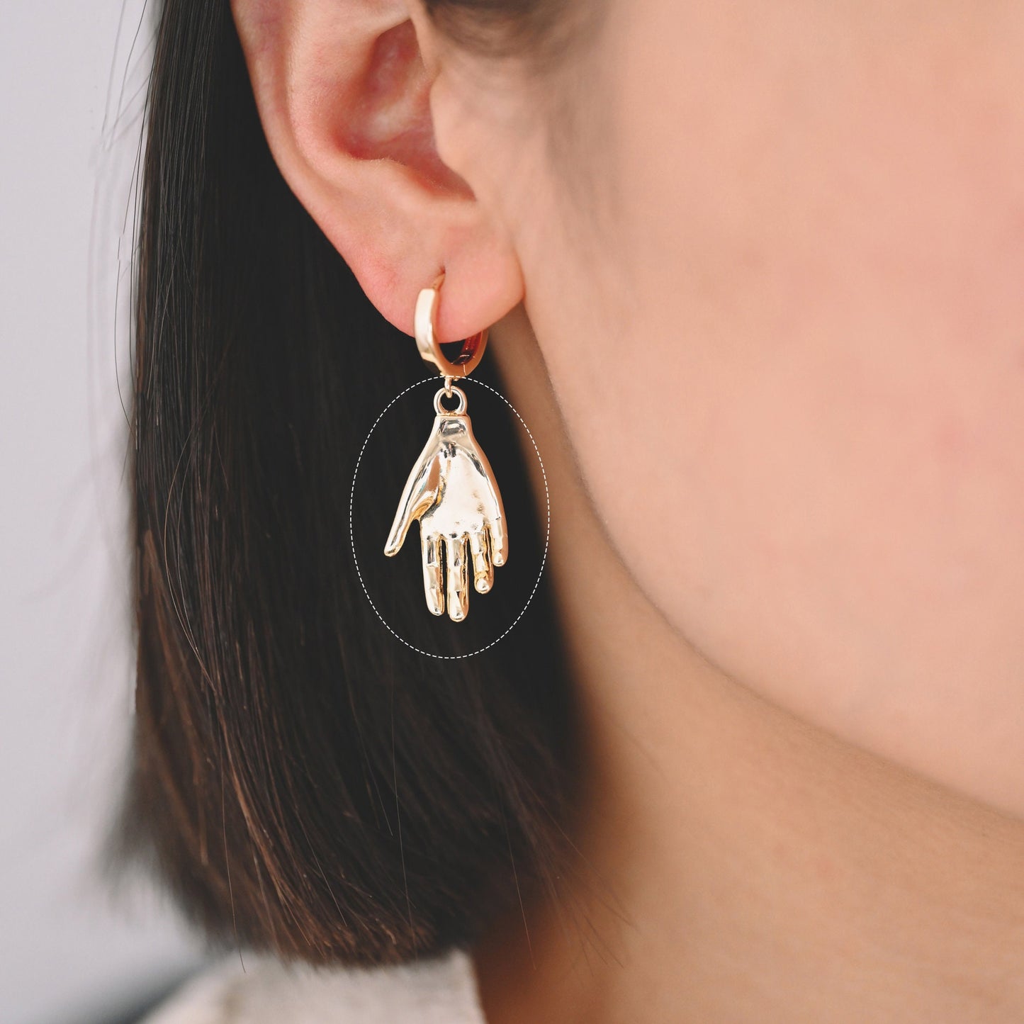 May include: Gold hoop earrings with a dangling hand charm.
