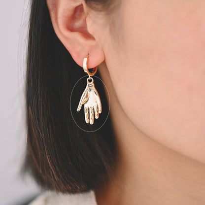 May include: Gold hoop earrings with a dangling hand charm.