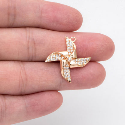 May include: A gold-toned pinwheel charm with clear rhinestones. The pinwheel has four blades and a center stone.