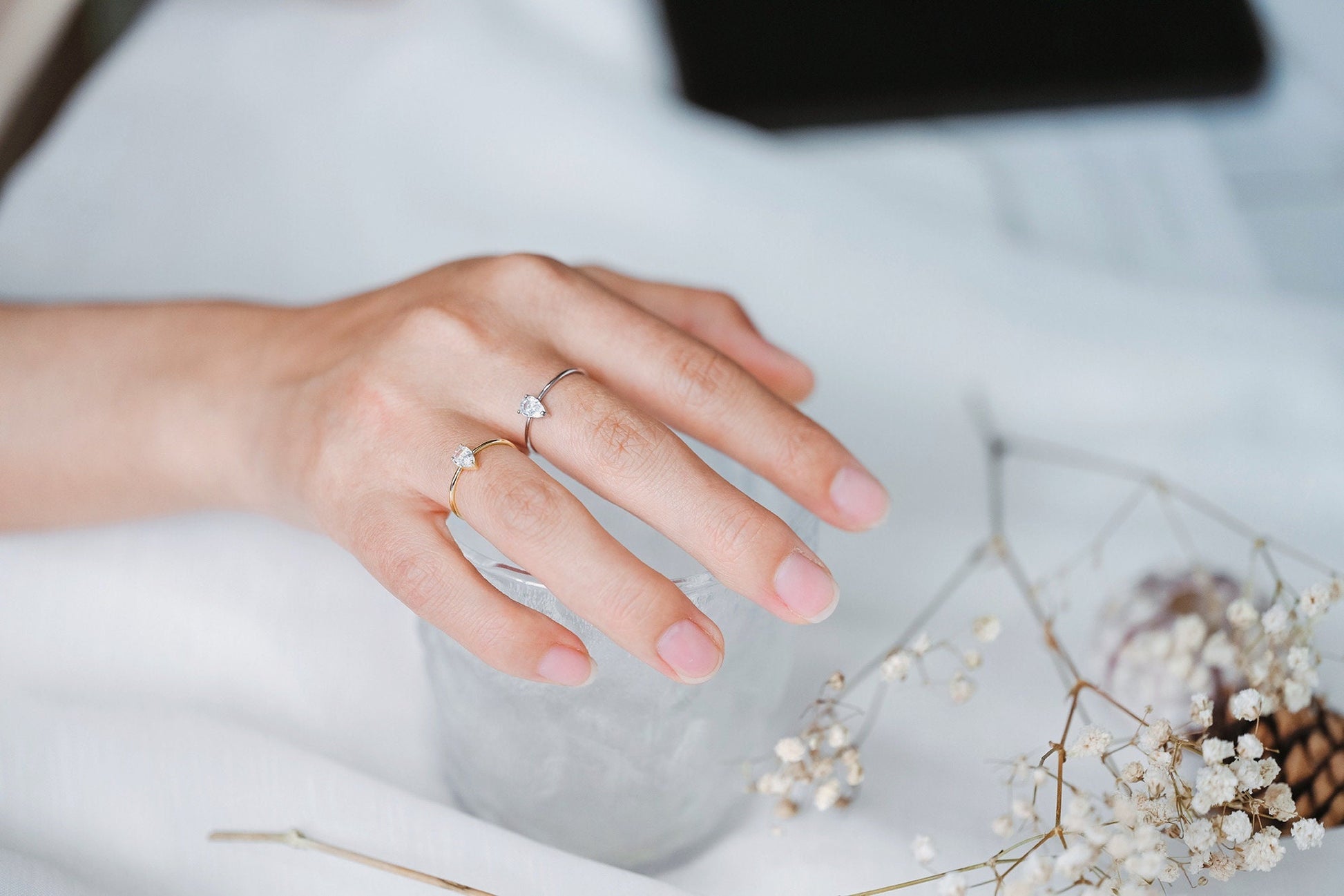 May include: Two simple rings with small clear stones on a finger. The ring on the index finger is gold, and the ring on the middle finger is silver.