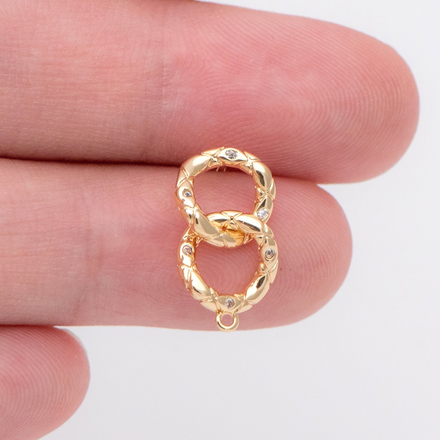 May include: A gold double ring charm with small clear stones around the edges. The charm has a loop at the bottom for attaching to a necklace or bracelet.
