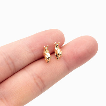 May include: Two small, gold-colored snail earrings. The earrings are detailed with a spiral shell design and delicate antennae. The earrings are shown on a light background.