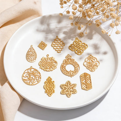 May include: A collection of gold-colored filigree charms in various shapes, including teardrops, squares, and floral designs, arranged on a white plate. The charms have intricate openwork patterns and are displayed with dried flowers.
