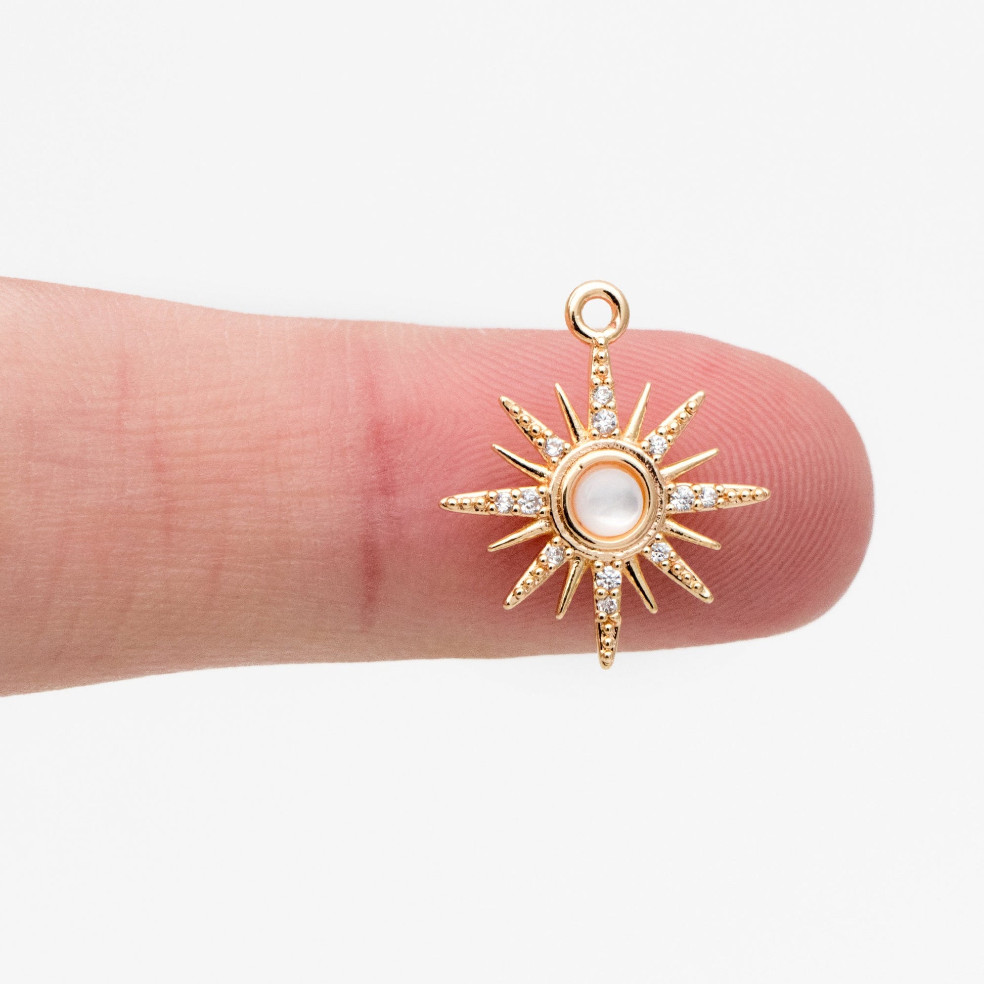 May include: Gold starburst charm with a white pearl center and clear crystal accents. The charm has a loop at the top for attaching to jewelry.