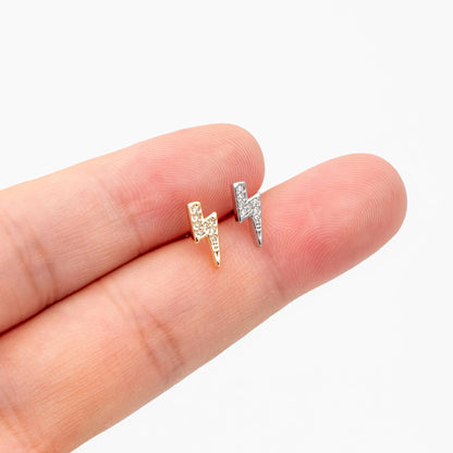 May include: Two small, stud earrings in the shape of lightning bolts. One is gold-toned, the other silver-toned, both encrusted with small, clear crystals. The earrings are displayed on a finger against a white background.