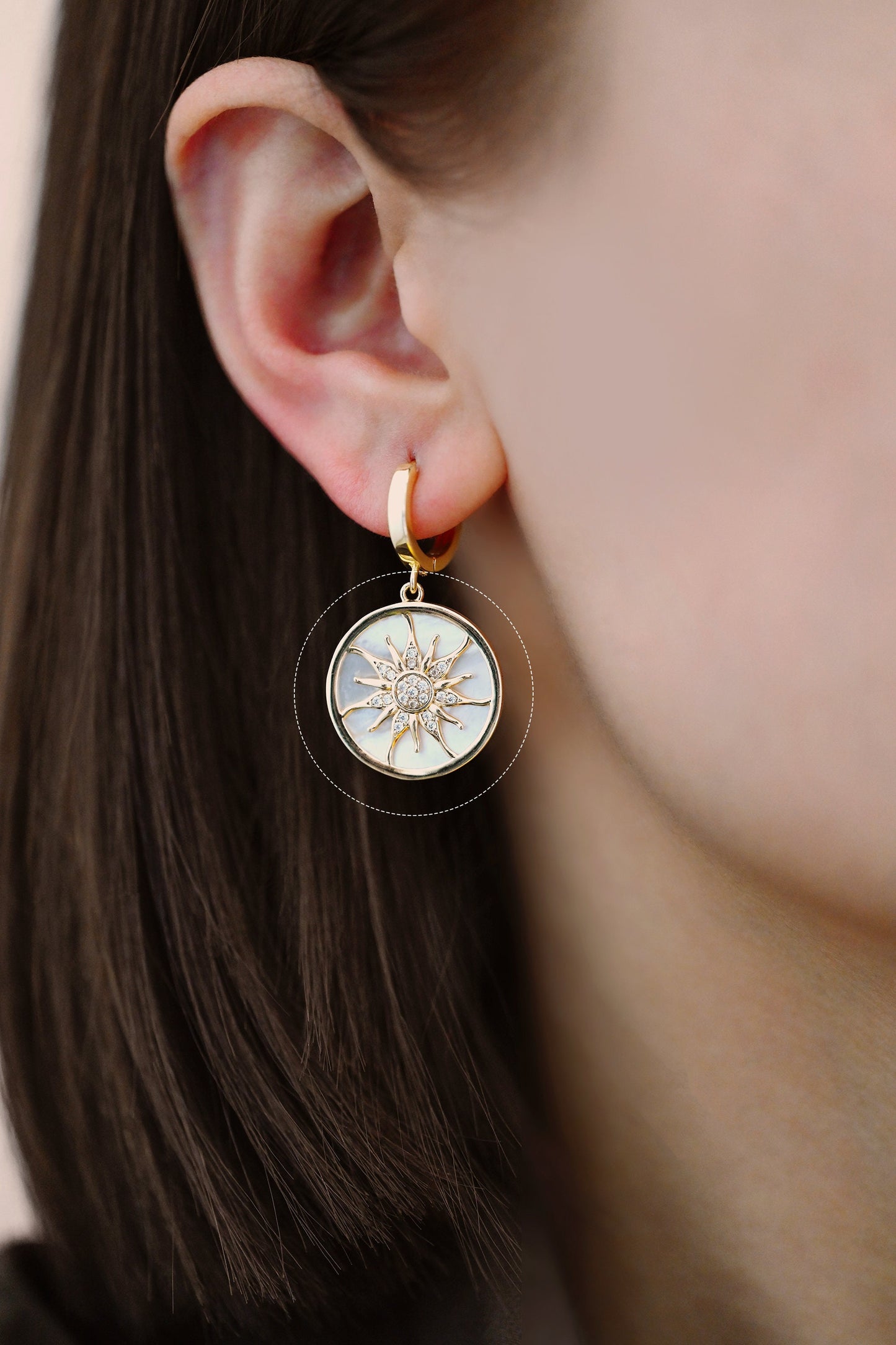 May include: Gold hoop earrings with a white mother-of-pearl sun pendant featuring a diamond-like center and gold rays.
