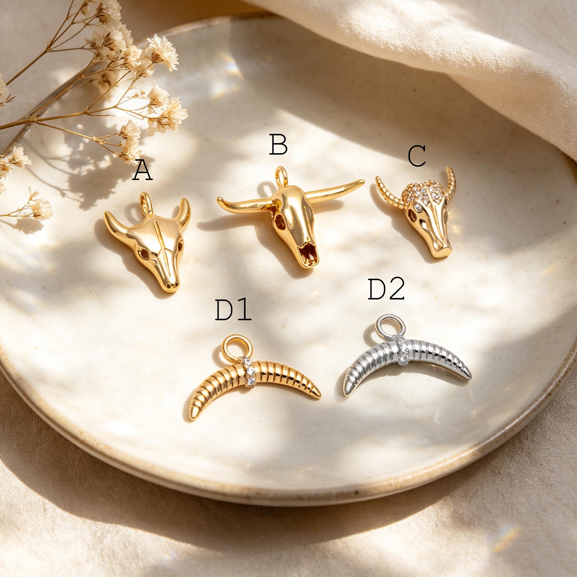 May include: A collection of gold and silver-toned bull and horn charms. The charms are in various styles, including a bull skull and crescent horn designs. Some charms are embellished with small, clear gemstones.